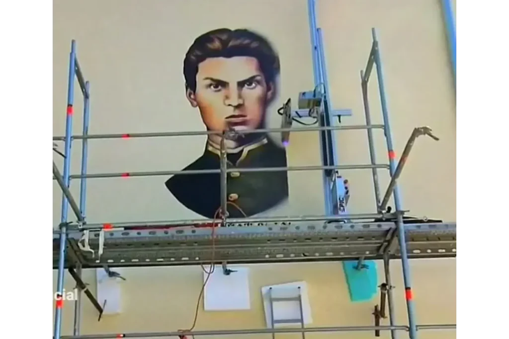 Wandgemälde eines jungen Mannes in historischer Uniform wird auf Hausfassade gemalt, Baugerüst im Vordergrund
