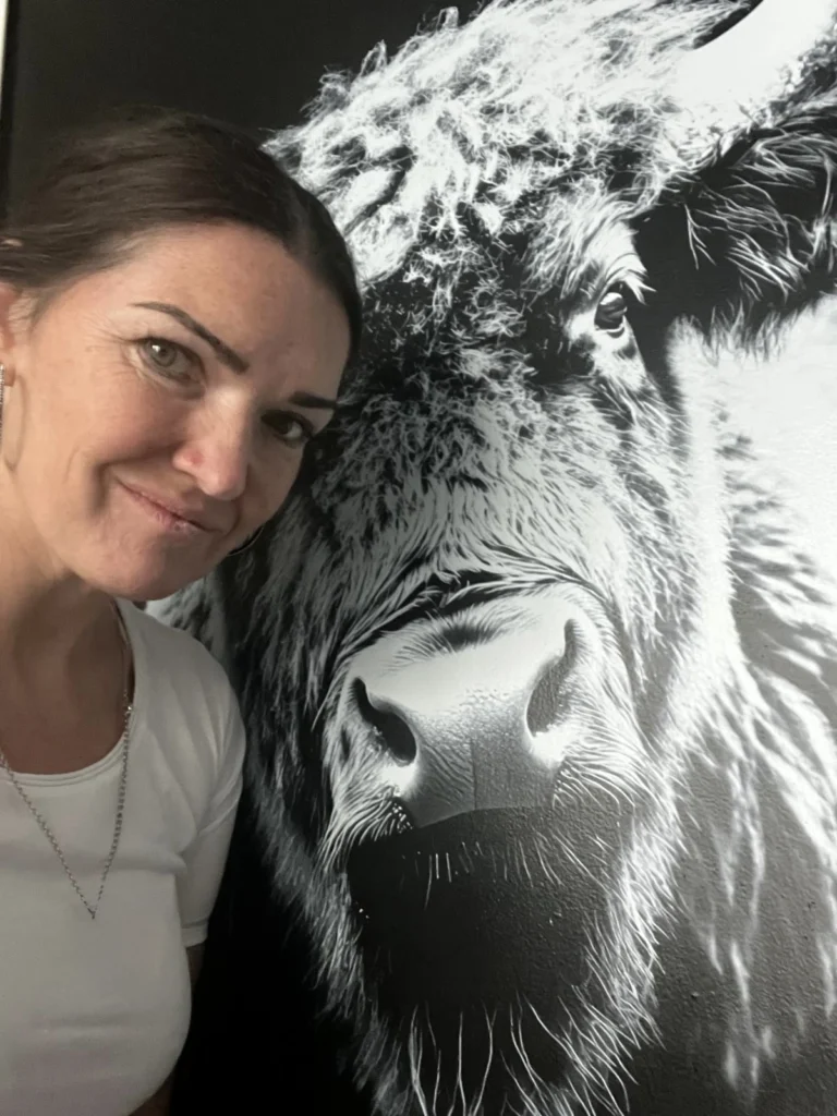 Frau mit braunem Haar posiert lächelnd vor schwarz-weißem Kunstdruck eines Bisons an der Wand