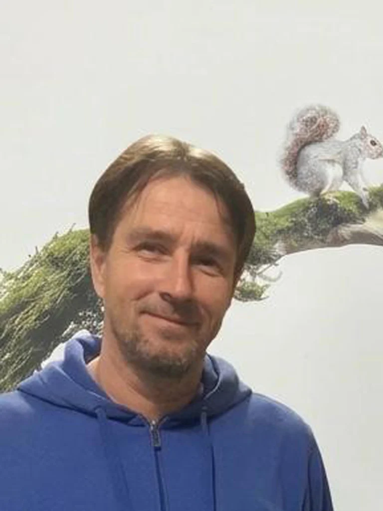 Mann in blauem Kapuzenpullover vor einem Baum mit Eichhörnchen auf einem Ast im Freien
